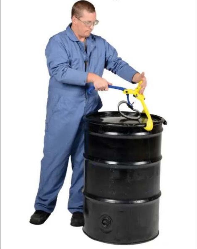 Worker in blue work uniform handling a yellow bucket with a tool, standing beside a black barrel (no text or symbols visible)