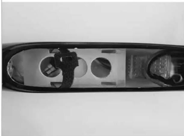 Top-down view of a transparent plastic device with internal circular cutouts and a small inset showing a person (no text or symbols visible)