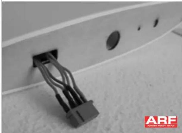 Close-up of a black cable connector inserted into a wall socket, with circular holes and a red 'ARF' logo in the corner (no readable text on main subject)