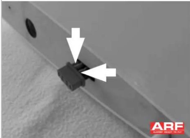 Close-up of a mechanical component with two white arrows pointing to a black connector (no text or symbols visible)
