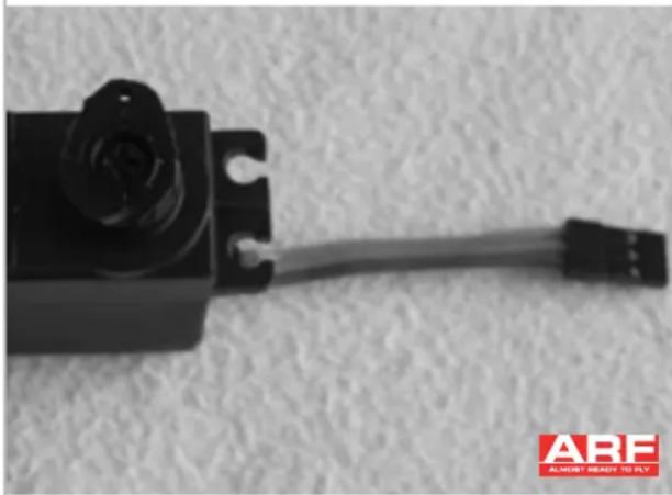 Close-up of a black mechanical component with a white cable, placed on a textured surface (no visible text or symbols)