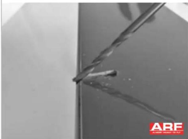 Close-up of a metal drill bit cutting through a metal sheet, with no visible text or symbols in the main image area.