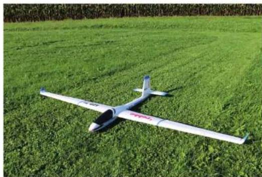 A small unmanned aerial vehicle (UAV) flying over a green agricultural field, no visible text or symbols.