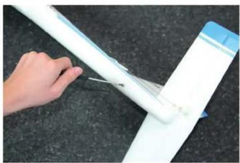 Hand holding a white cylindrical object with a thin wire, placed on a dark surface (no text or symbols visible)