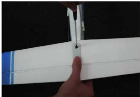 Close-up of a hand holding a white propeller airplane wing against a black background (no text or symbols visible)