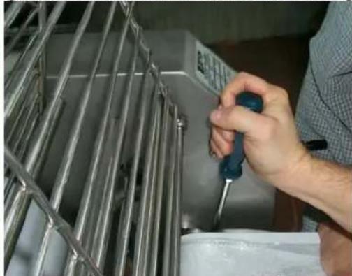 Person using a screwdriver to adjust or install a metal rack inside a container (no visible text or symbols)