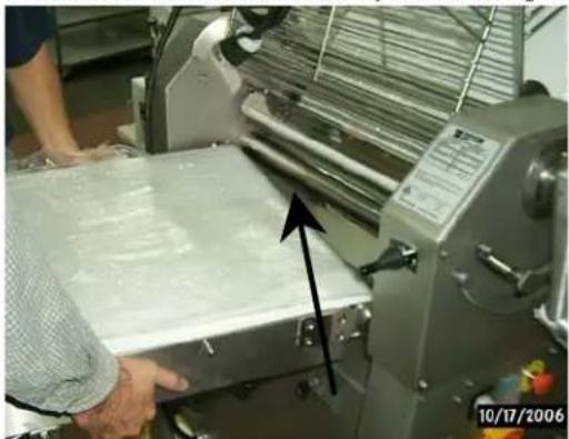 Person operating a large mechanical printing machine with a paper sheet being cut (no visible text or symbols)