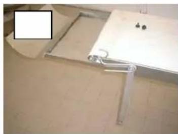 Close-up of a white metal shelf support bracket mounted on a tiled floor, with small black components visible (no text or symbols)