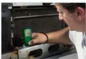 Person using a green handheld device to adjust or install electronic equipment (no visible text or symbols)