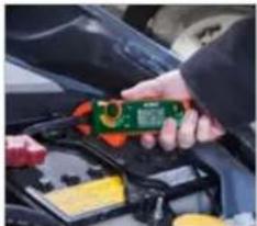 Close-up of hands using a multimeter on a car engine, no visible text or symbols