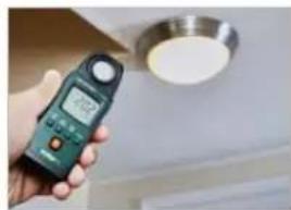 Hand holding a digital multimeter displaying a reading on a ceiling fixture (no visible text or symbols)