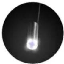 Circular black-and-white image showing a bright, glowing object against a dark background, possibly a celestial body or light source.