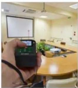 Person holding a smartphone in a meeting room with a projection screen and table (no visible text or symbols)
