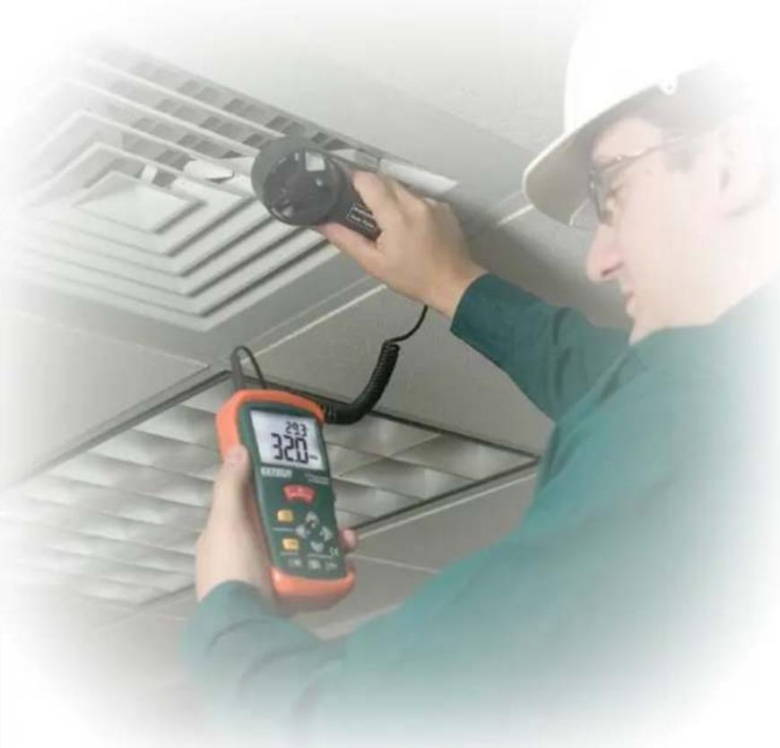 Technician inspecting air quality measurement equipment with a digital thermometer and clamp (no visible text or symbols)