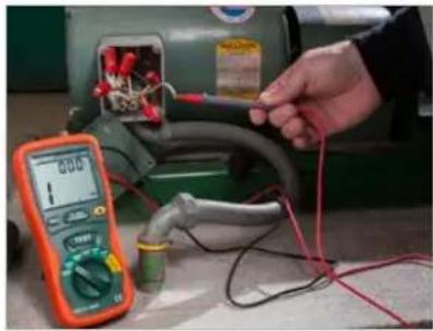 Person using a multimeter to test electrical wiring with components in a workshop (no visible text or symbols)