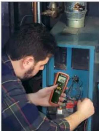 Man in work uniform inspecting a blue industrial machine with digital meters (no visible text or symbols)