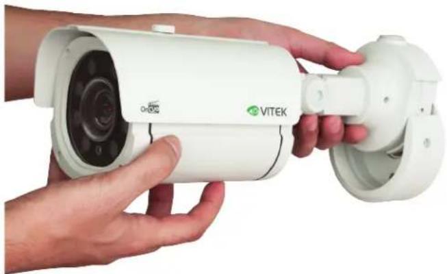 Close-up of hands holding a white VITEK security camera with a cylindrical connector (no visible text or symbols on the device itself)