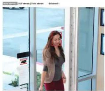 Woman standing in front of a glass-framed room with a laptop and monitor (no visible text or symbols)