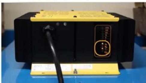 Close-up of a black and yellow electronic device with a black cable and a yellow control panel, placed on a blue surface (no visible text or symbols)