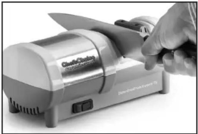 Hand holding a knife next to a cooking machine (no visible text or symbols on the device itself)