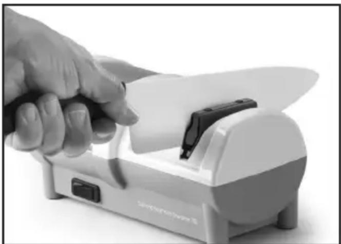 Hand using a handheld device to cut a knife into a slot (no visible text or symbols)