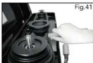 Close-up of a hand operating a mechanical device with a cylindrical component and attached cable (no visible text or symbols)