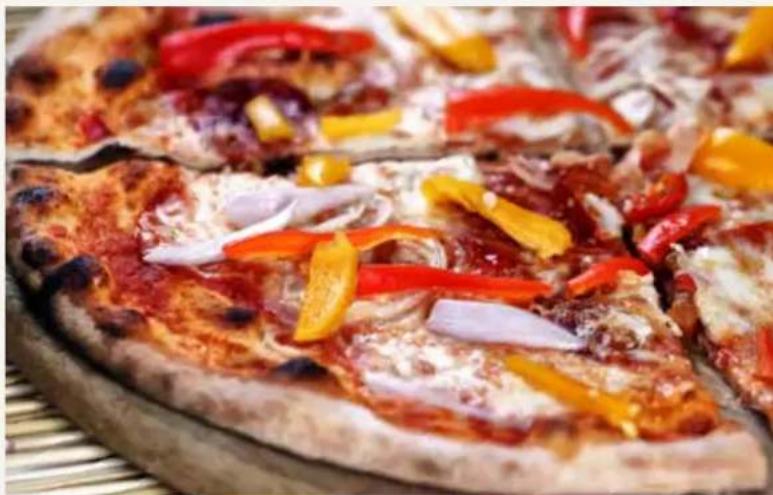 Close-up of a colorful pizza with red sauce, white cheese, and chili peppers on a bamboo mat (no text or symbols visible)