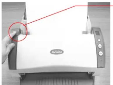 Hand holding a white electronic device with a red arrow pointing to a button, no visible text or symbols on the device itself.