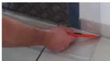 Close-up of a hand using a red tool to cut or mark a white surface on a tiled floor (no text or symbols visible)