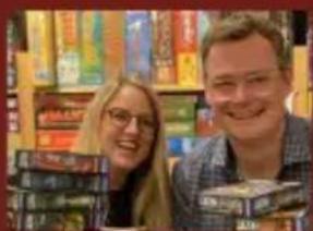 Two smiling people holding stacked books in a bookstore (no visible text or signage)