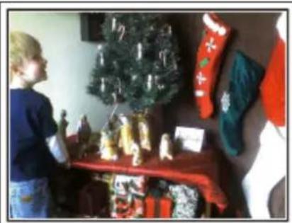 Child standing beside a red table with Christmas decorations including a Christmas tree, socks, and stuffed goods (no visible text or symbols)