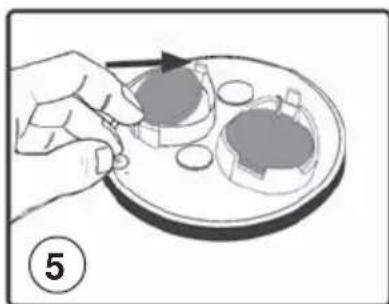 Illustration of a hand placing a small object onto a plate with two circular components, no text or symbols present.