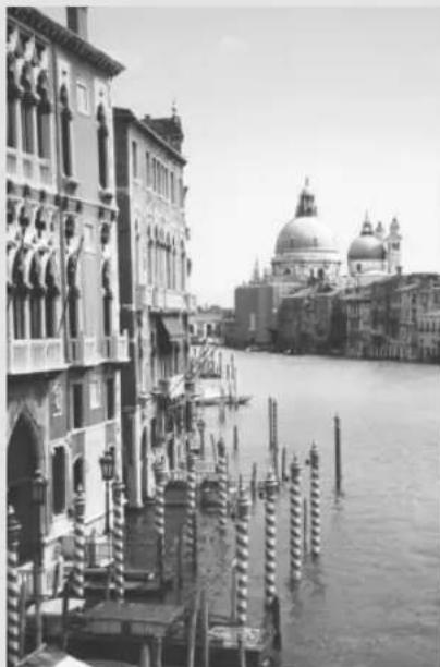 Black-and-white photo of a canal scene with historic buildings and a large domed building in the background (no visible text or symbols)