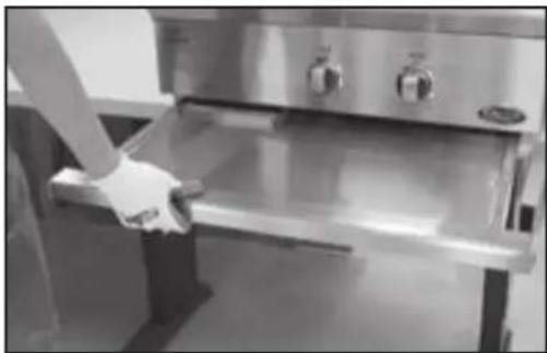 Person holding a stainless steel kitchen appliance with control knobs (no visible text or symbols)