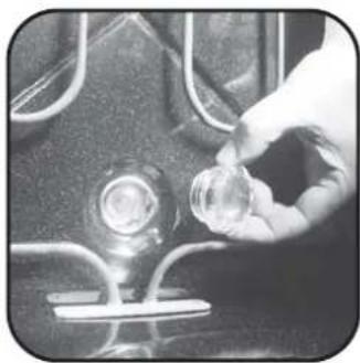 Close-up of a hand holding a small transparent object over a dark surface with curved lines and a central circular feature (no text or symbols visible)
