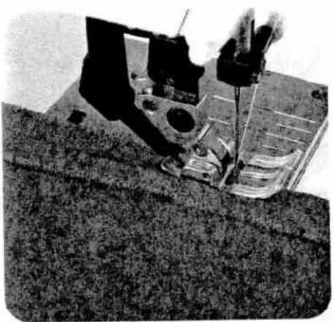 Black-and-white photo of a sewing machine needle stitching fabric, no visible text or symbols