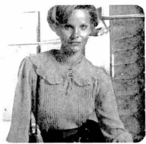 Black-and-white photo of a woman in vintage clothing, standing indoors near a window (no visible text or symbols)