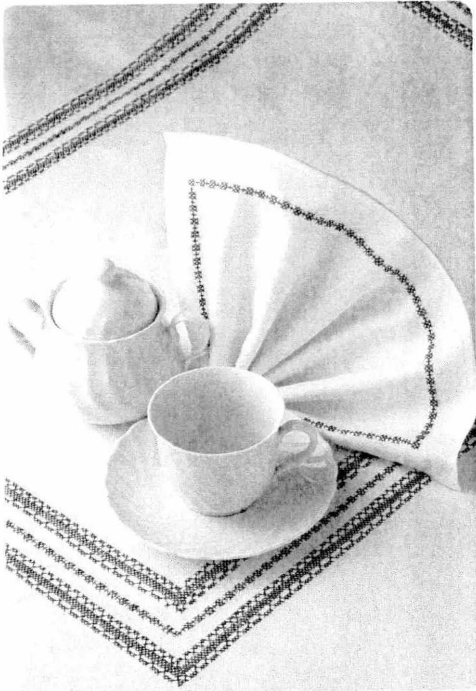 Black-and-white photo of a tea set with saucers and a teacup on a patterned tablecloth, no visible text or symbols.