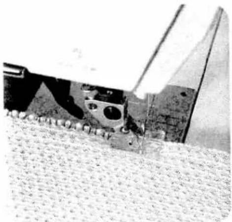 Close-up of a mechanical component with circular holes and a triangular base, resting on a textured surface (no visible text or symbols)