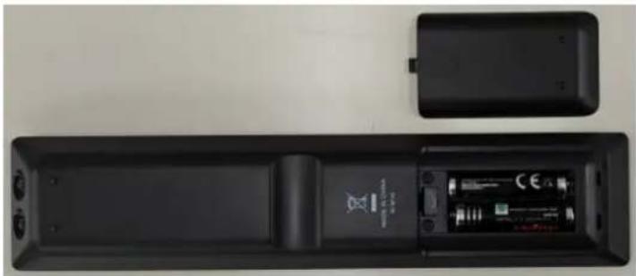 Top-down view of a black remote control box with battery and speaker, showing front panel and side casing (no text or symbols visible)