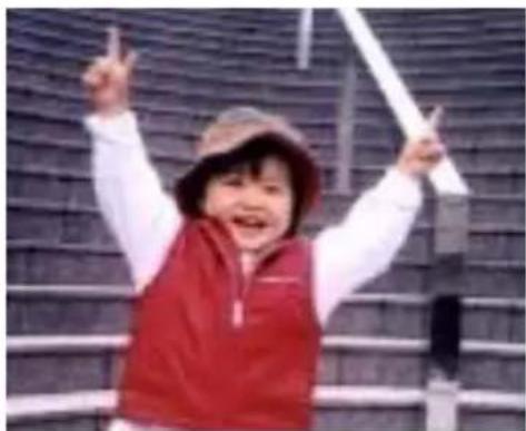 A smiling child in a red vest and hat, raising one arm with raised index finger, against a blurred outdoor background (no text or symbols visible).