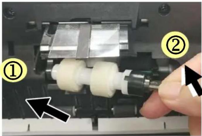 Close-up of a mechanical assembly showing a finger pressing a component with numbered callouts (① and ②) and an arrow indicating direction.