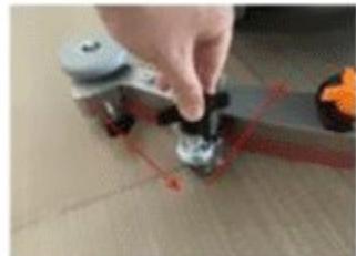 Close-up of a hand pressing a small black object on a wooden surface, with a small inset showing orange objects (no text or symbols visible)
