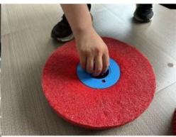Close-up of a hand pressing down on a red circular textured surface with a blue circular base (no text or symbols visible)