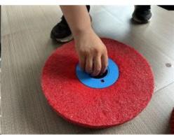 Close-up of a hand pressing down on a red circular textured surface with a blue circular base (no text or symbols visible)