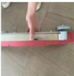 Close-up of a hand pressing down on a red and white metal object on a wooden floor (no text or symbols visible)