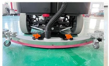 Close-up of a cleaning or cleaning machine on a tiled floor, showing wheelbars and orange components (no visible text or symbols)