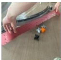 Close-up of hands holding a red and black object on a wooden floor, with small figurines nearby (no visible text or symbols)