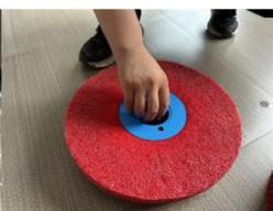 A person pressing down on a red circular surface with a blue base, on a tiled floor (no text or symbols visible)
