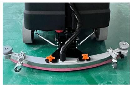 Close-up of a cleaning or cleaning robotic device with attached tubing and orange buttons, mounted on a curved platform (no visible text or symbols)